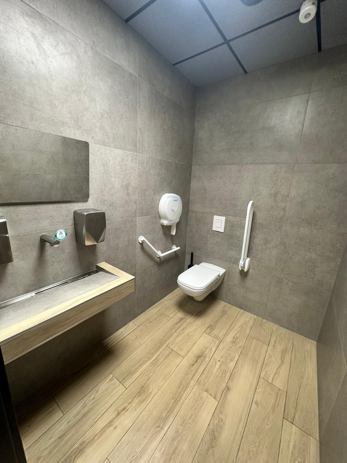 Toilettes accessibles avec barres d'appui, lavabo suspendu et distributeur de gel hydroalcoolique mural.
