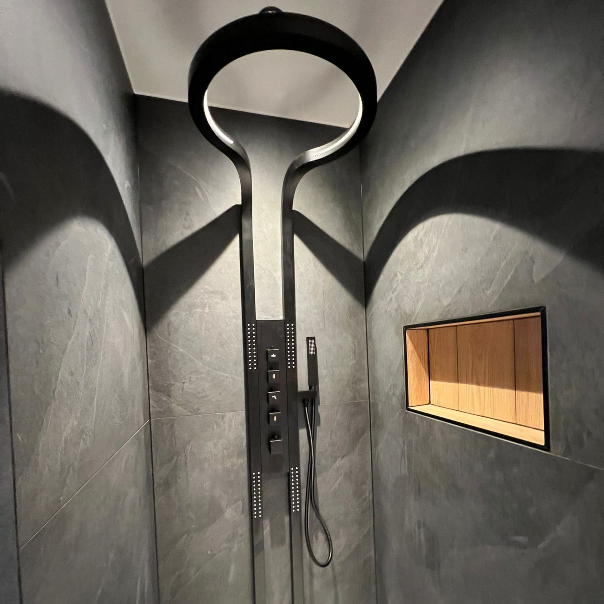Pommeau de douche noir avec éclairage circulaire dans une douche carrelée gris foncé.
