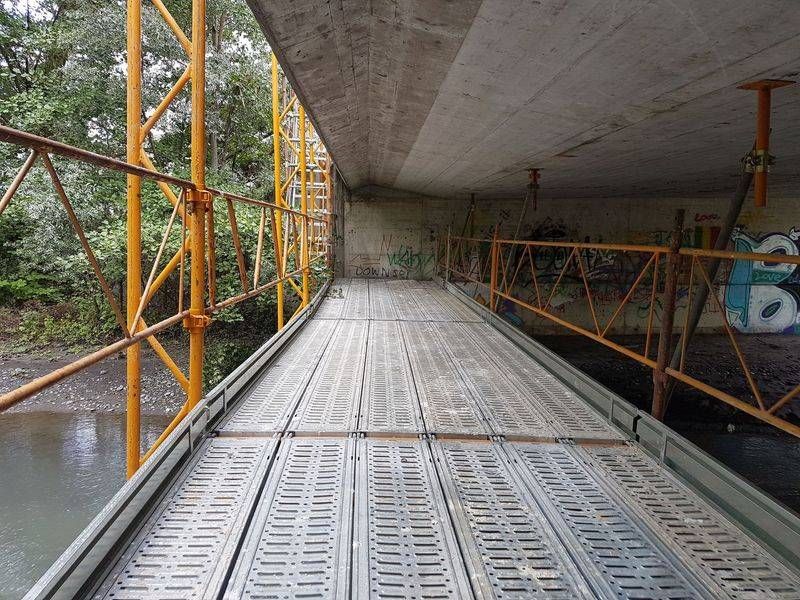 Un pont avec des échafaudages et un tablier en bois au-dessus d'un plan d'eau.