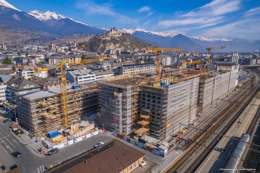 Un grand bâtiment en construction avec des échafaudages et des camions garés devant.