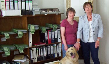 Zwei Frauen stehen neben einem Hund in einem Büro