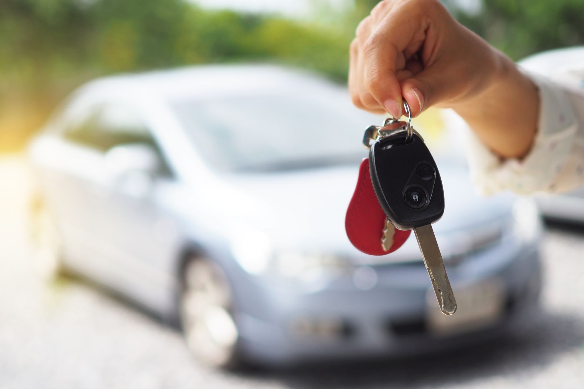 Main tenant des clés de voiture avec un porte-clés rouge devant une voiture argentée, arrière-plan flou