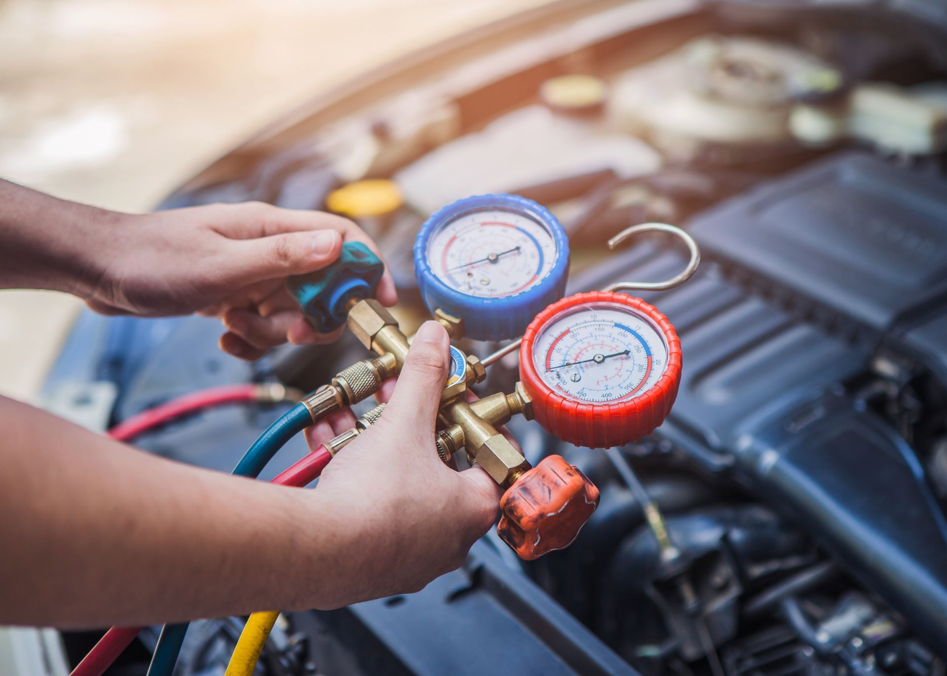 Des mains connectent des manomètres au système de climatisation d'une voiture dans un garage.