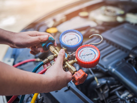 Mains manipulant des manomètres et des tuyaux sur le moteur d'une voiture lors de l'entretien de la climatisation
