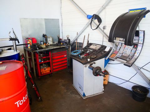 Coin atelier avec outils, coffre à outils rouge, support de roue de vélo et établi noir dans un petit garage.