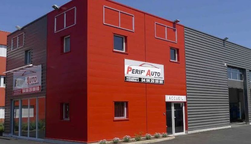 Bâtiment commercial rouge avec une enseigne PERIF AUTO et une extension industrielle grise.