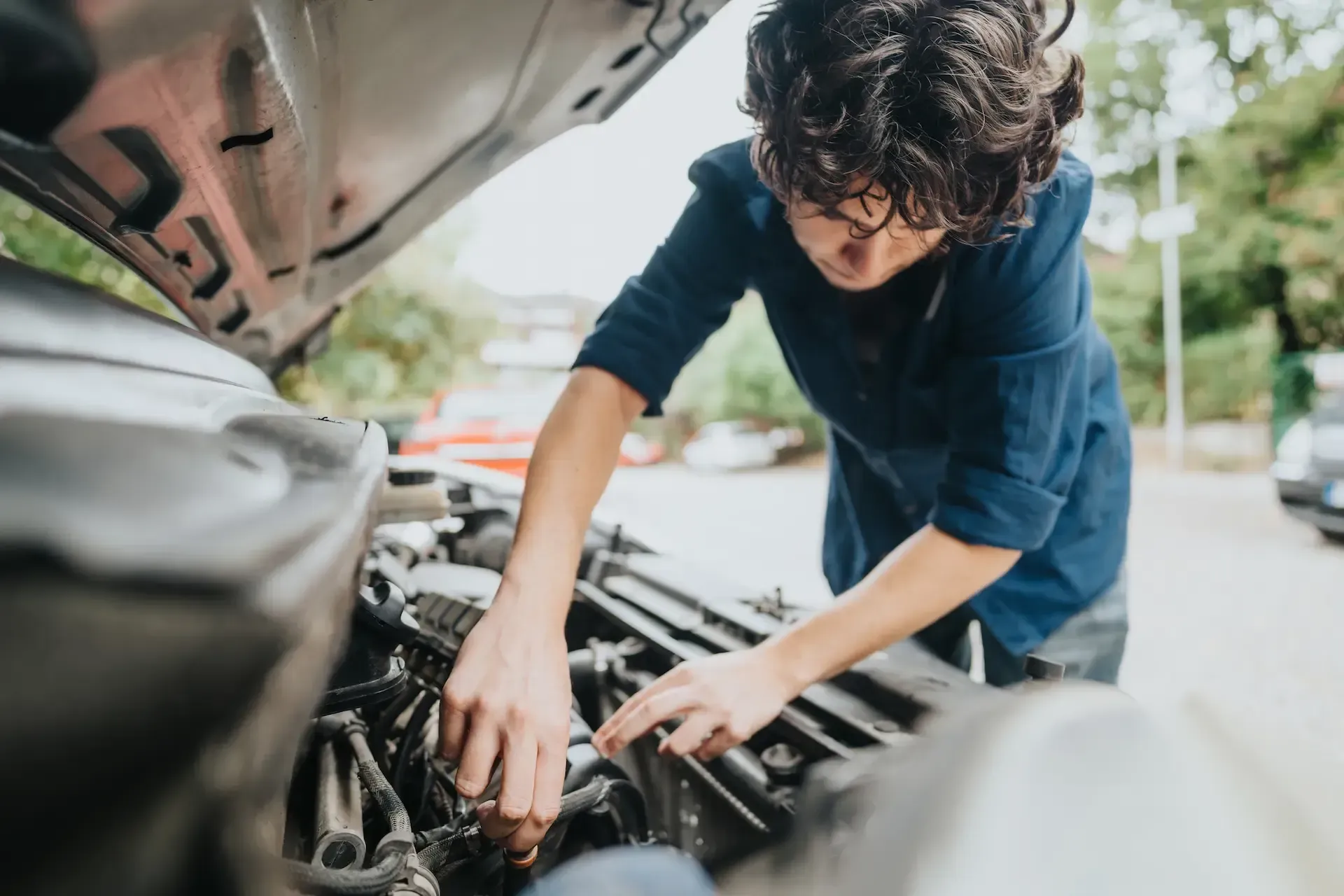 Persona con cabello rizado mirando el motor de un automóvil con el capó abierto.