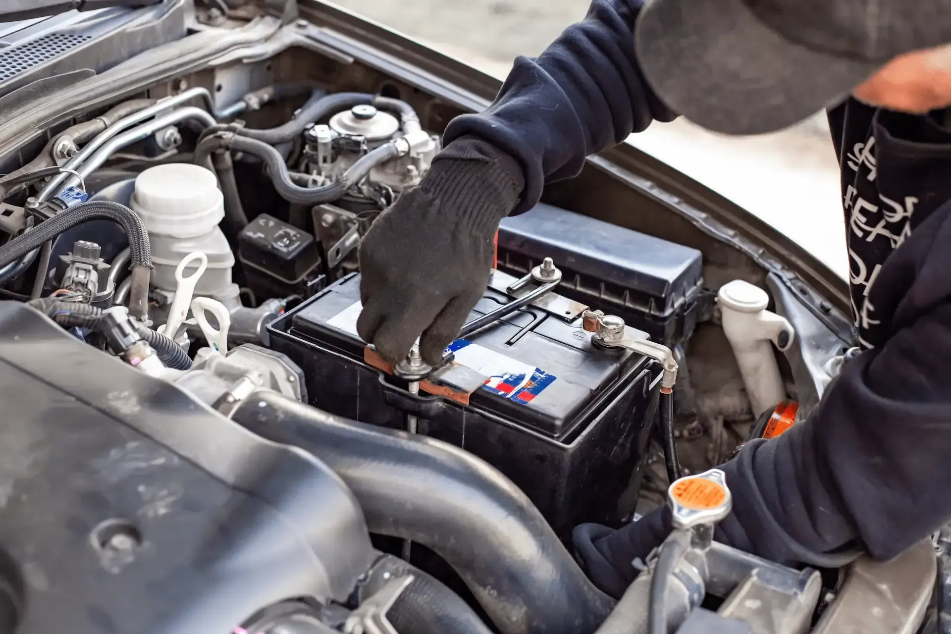 Mecánico trabajando en la batería del automóvil en el compartimiento del motor, usando guantes.