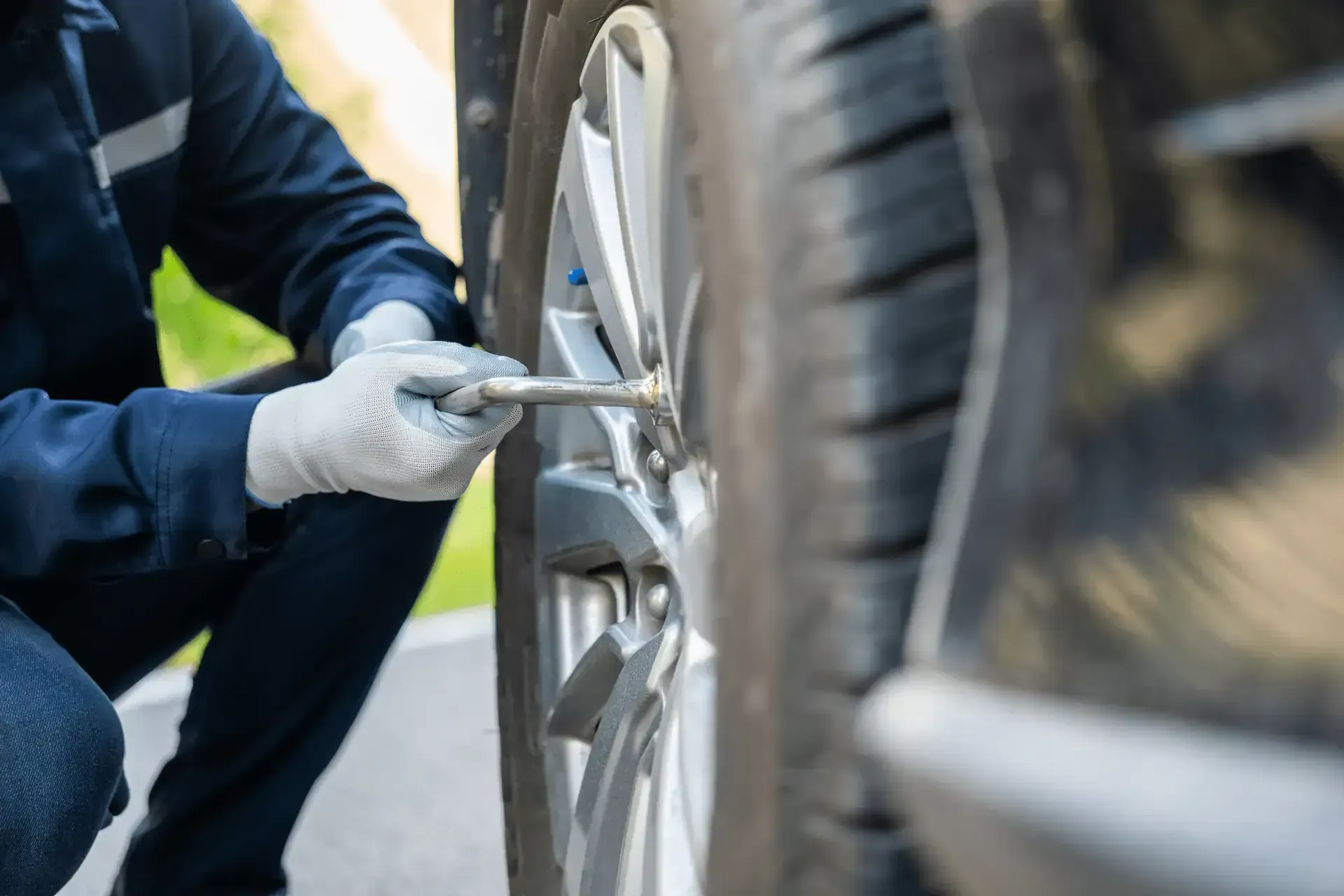 Un mecánico con uniforme azul utiliza una llave inglesa para aflojar las tuercas de un neumático de automóvil.