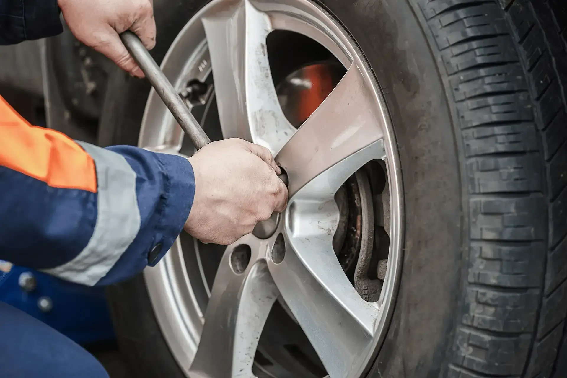 Mecánico que usa una llave para aflojar las tuercas de un neumático de automóvil, preparándose para un cambio de neumático.