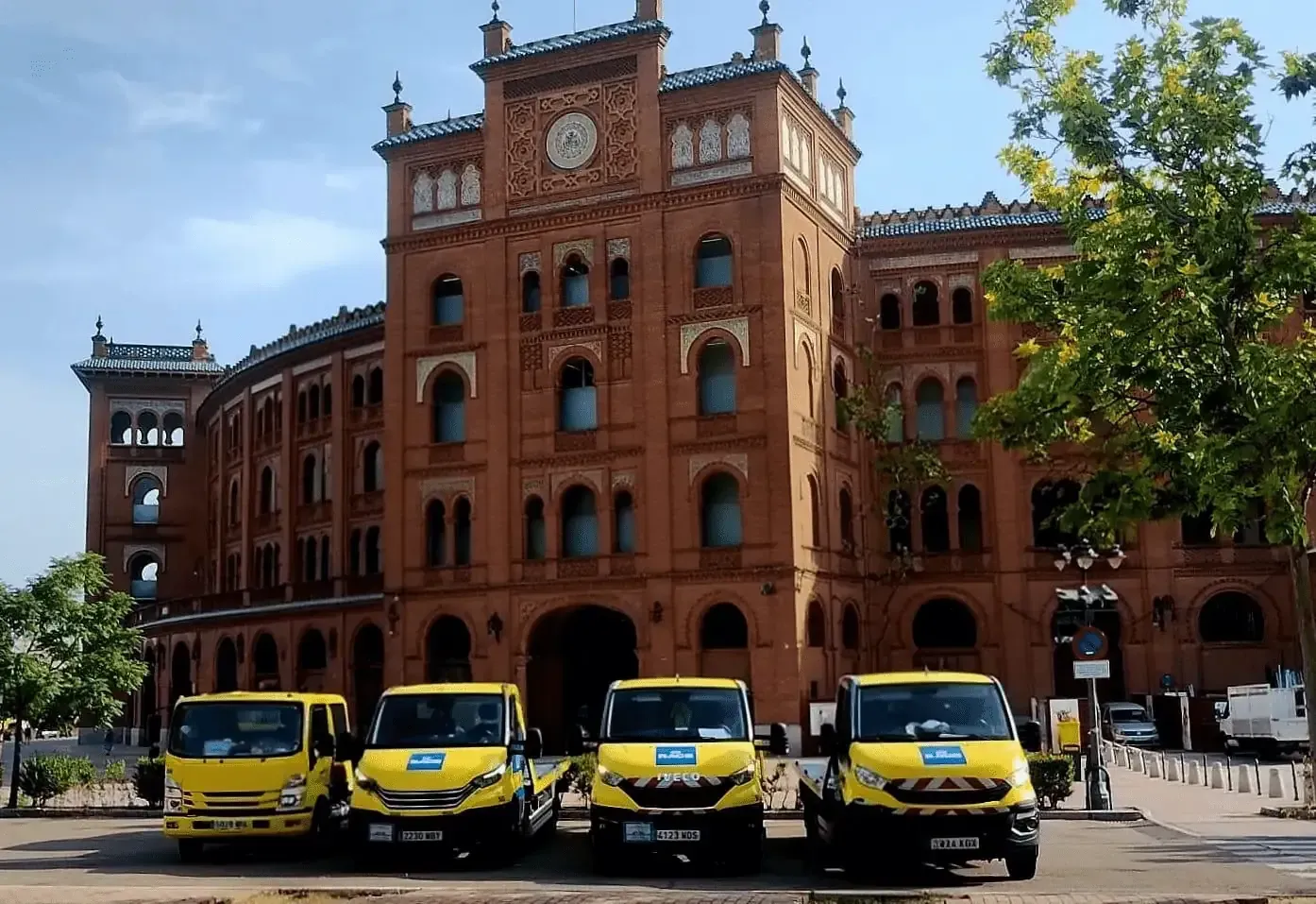Grúa con una caja blanca de alquiler sobre la plataforma. La grúa tiene detalles en amarillo y azul. Exterior.