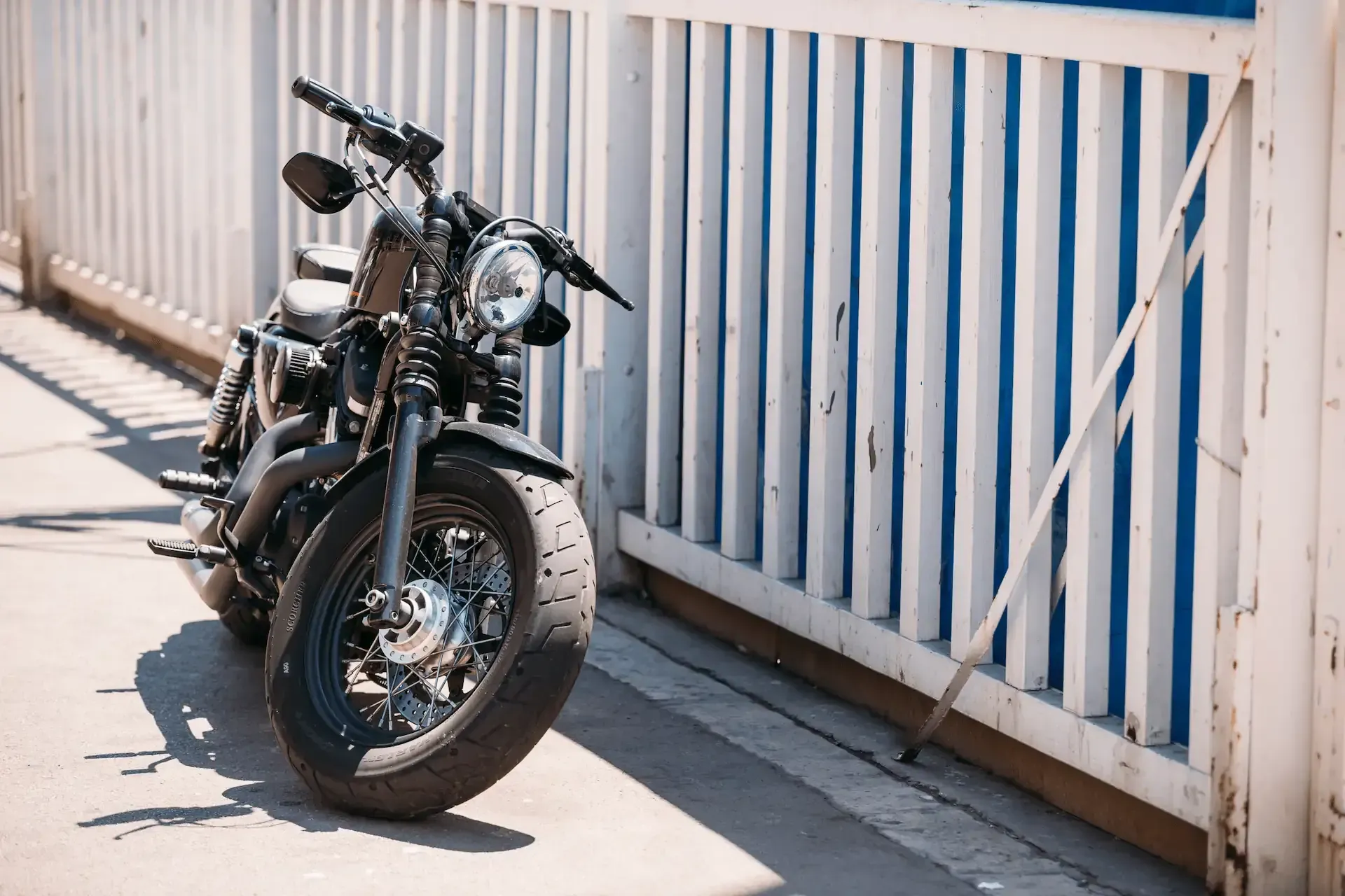 Motocicleta negra estacionada junto a una valla de madera blanca y azul en un día soleado.