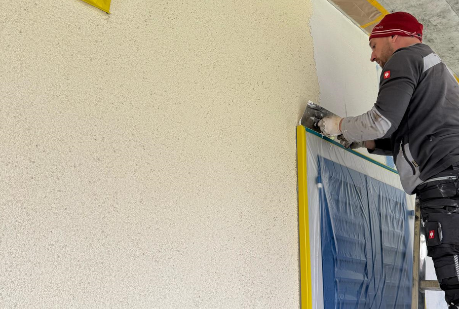 Ein Mann steht auf einer Leiter und streicht eine Wand.