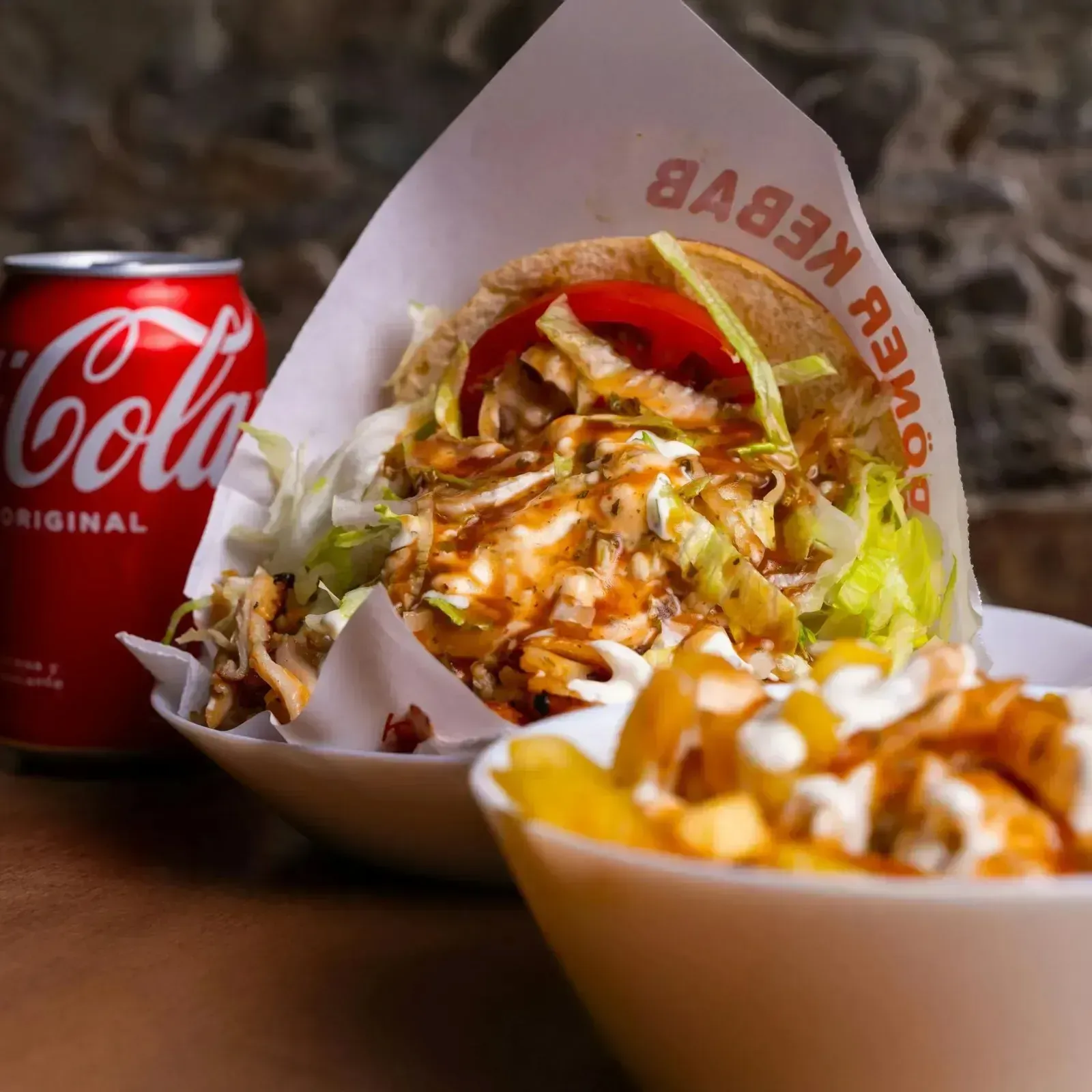 Wrap griego con lechuga y salsa junto a una lata de Coca-Cola, con patatas fritas en primer plano.