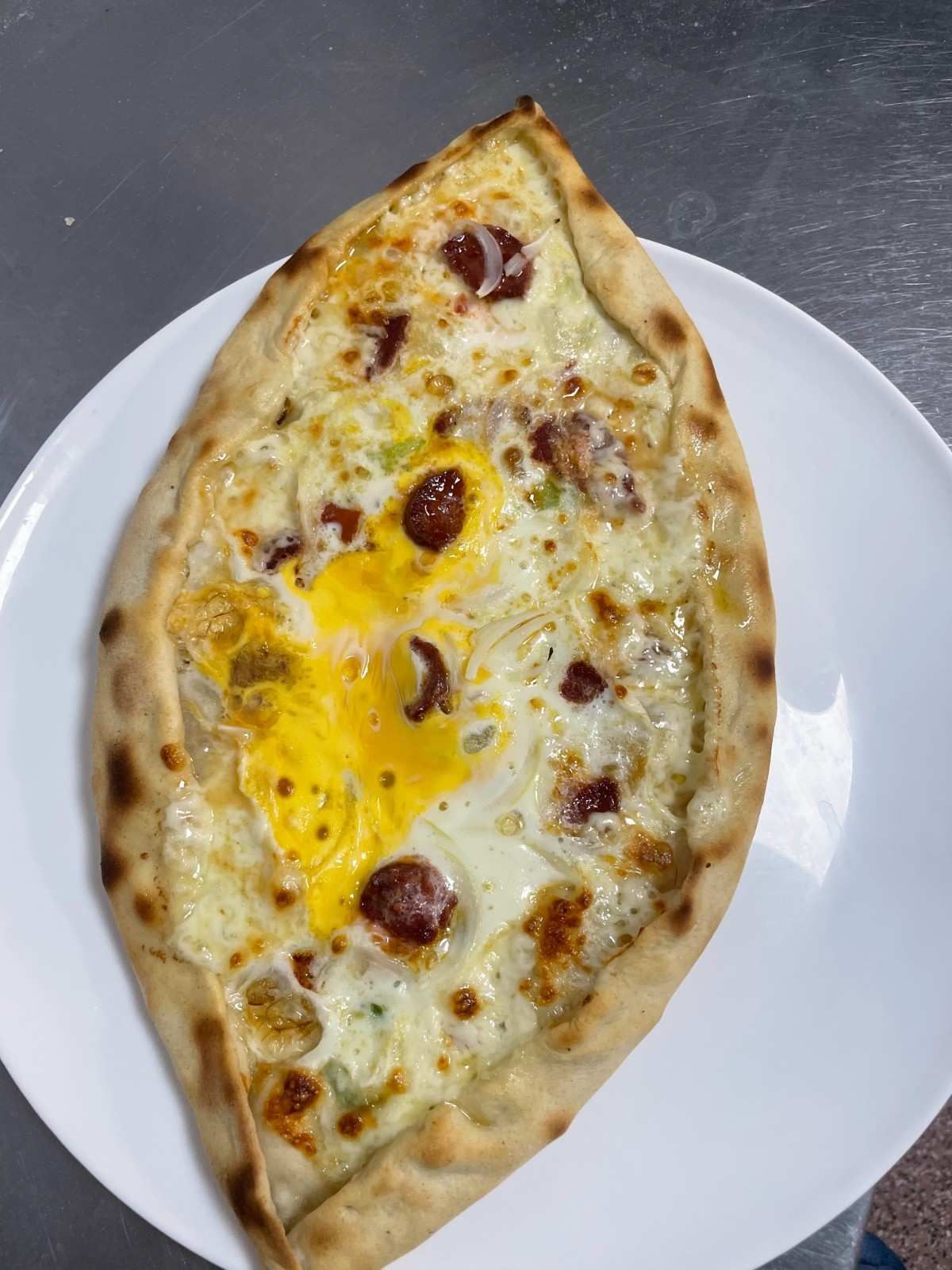 Plato ovalado blanco con un pan plano horneado en forma de barco cubierto con queso derretido y manchas doradas.