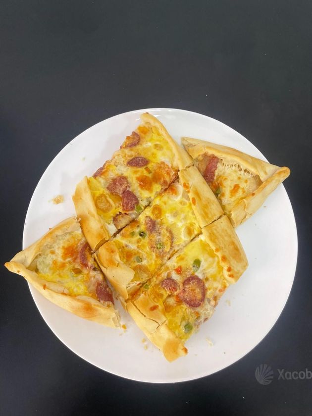 Pizza con queso en rodajas sobre un plato blanco con fondo oscuro.