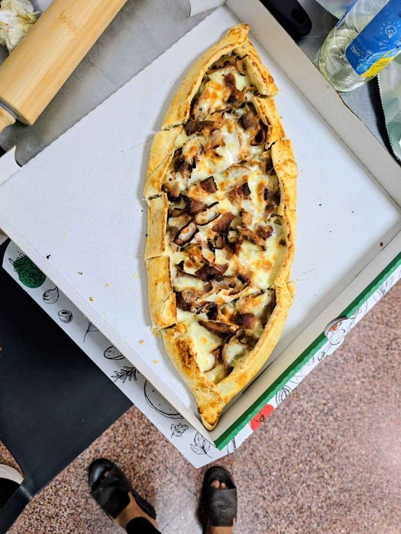 Pizza ovalada alargada en una bandeja con queso derretido y aderezos dorados sobre una encimera.