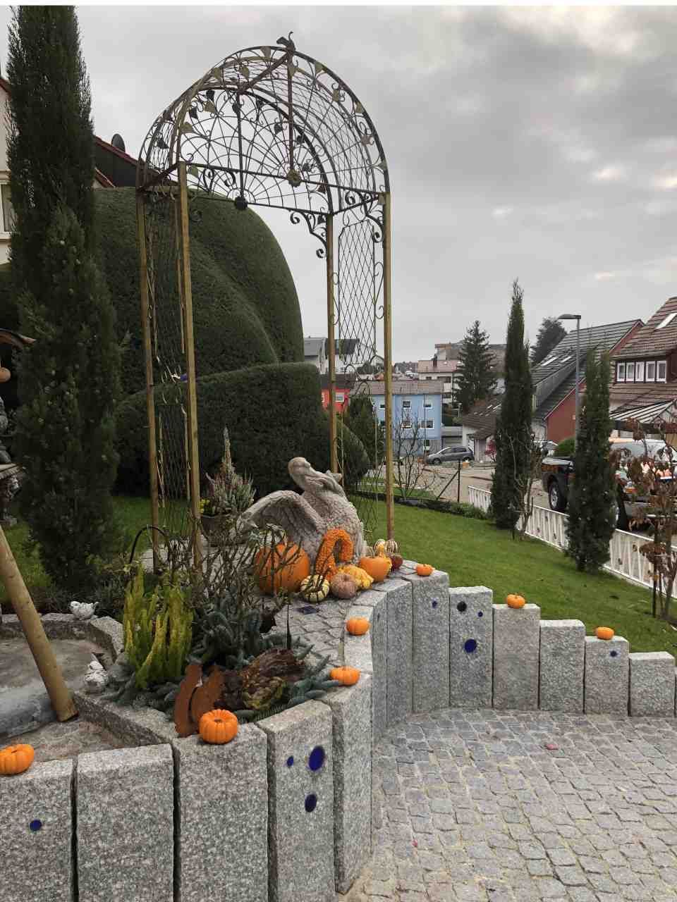 Gartengestaltung mit niedriger Steinmauer, Rasen, Kürbissen und Pelikanfigur