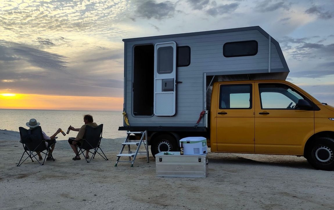 Ein Paar sitzt neben einem Wohnmobil am Strand.