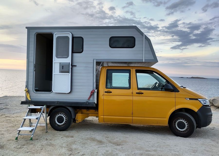 Am Strand parkt ein gelber Lastwagen mit einem Wohnwagen darauf.