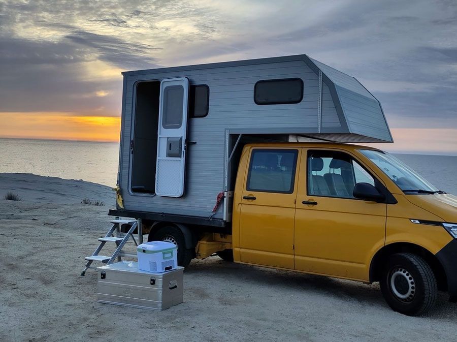 Am Strand parkt ein gelber Lastwagen mit einem Wohnwagen darauf.