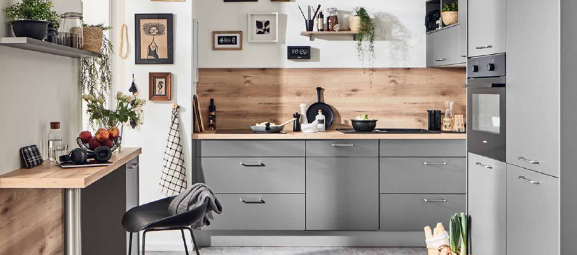 Moderne graue Küche mit Holzrückwand, schwarzem Stuhl, Einbaugeräten sowie kleinen Pflanzen und Dekorationselementen.