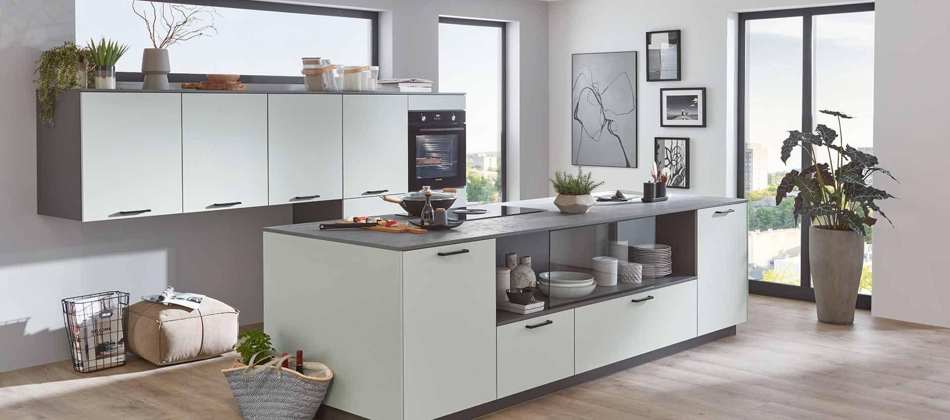 Moderne weiße Küche mit Kochinsel, Schränken, Pflanzen und großen Fenstern in einem hellen Raum