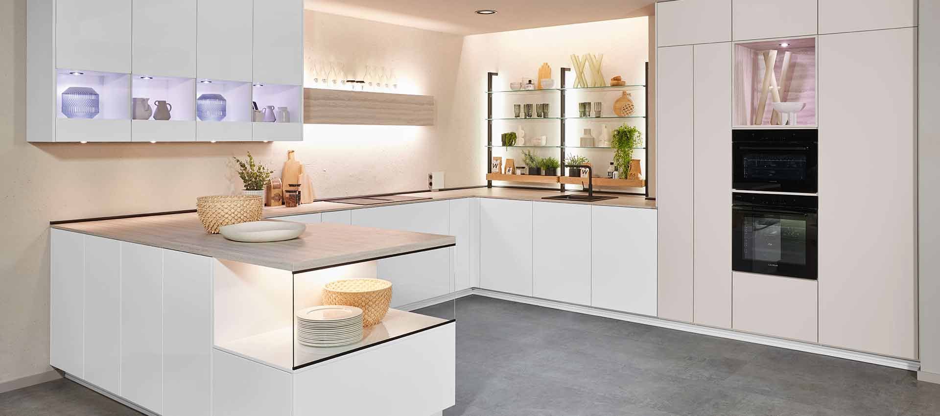 Moderne weiße Küche mit Kochinsel, Einbaubackofen, Arbeitsplatten aus Holz und warmer Unterbaubeleuchtung