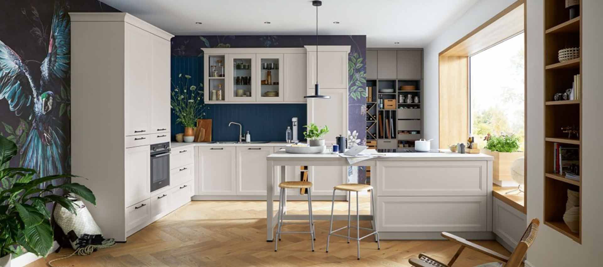 Helle, moderne Küche mit blauen Schränken, weißer Kochinsel, Esstisch und Sonnenlicht durch große Fenster