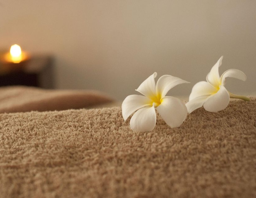 Fleurs de frangipanier blanches sur une serviette de spa, à côté d’une bougie à la lueur douce