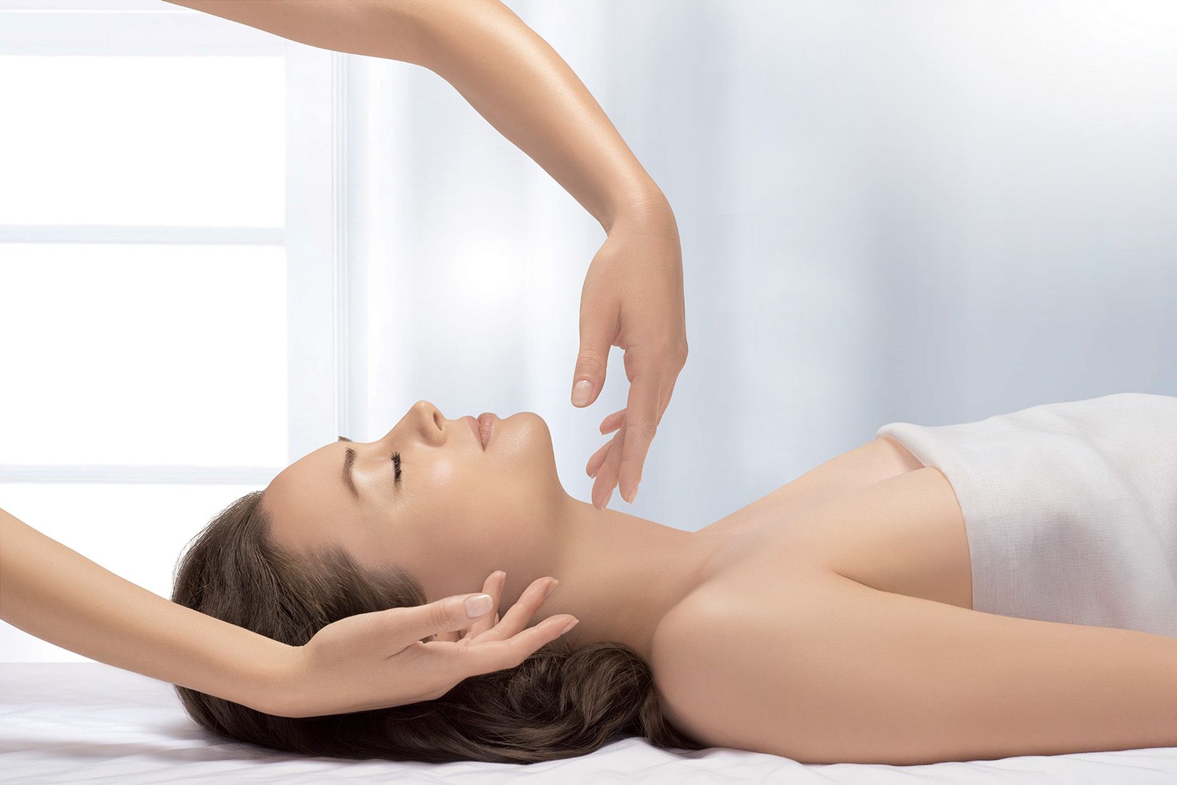 Une masseuse prodiguant un soin du visage à une femme allongée dans une salle de spa
