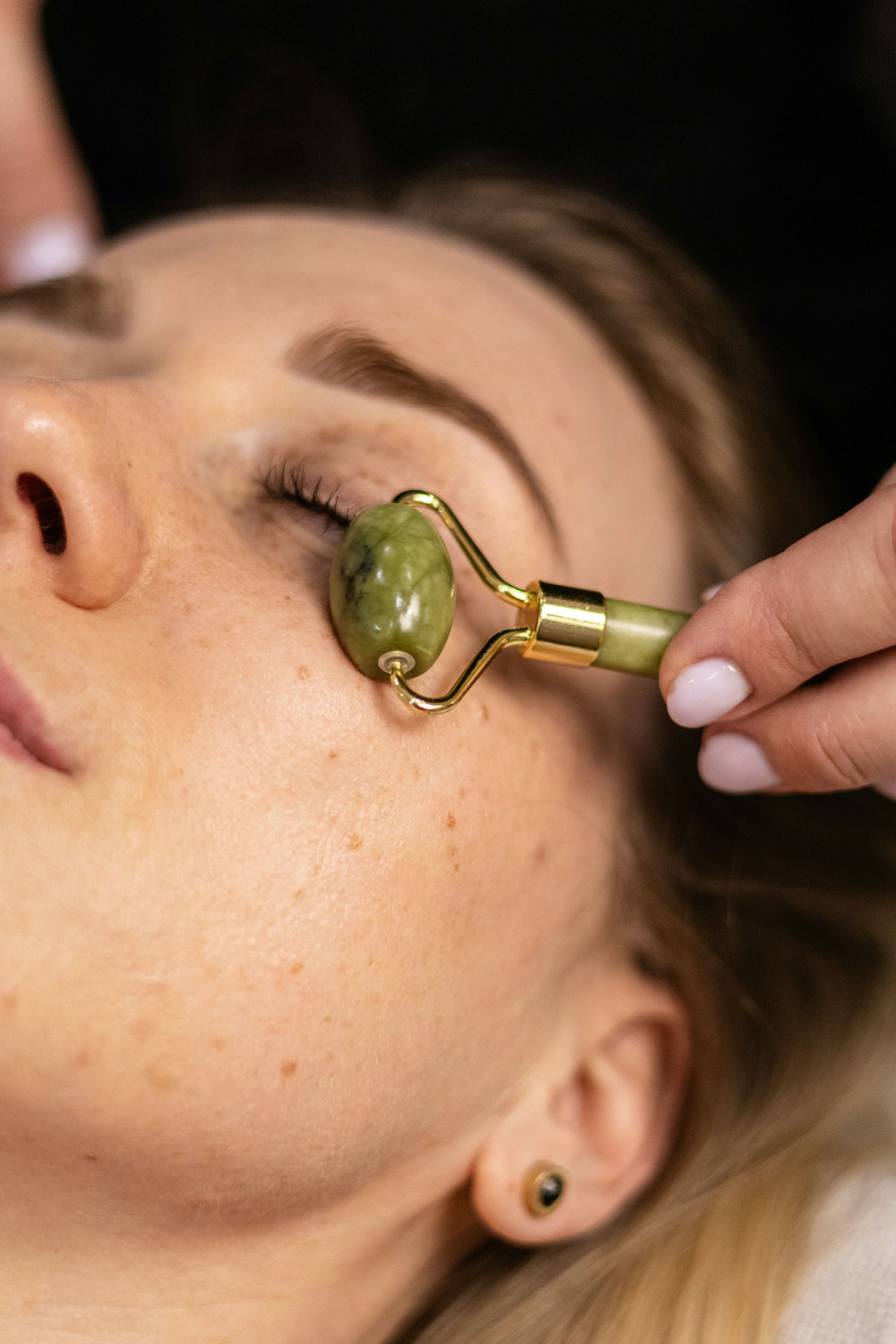 Femme recevant un massage du visage avec un rouleau en jade vert sur la joue