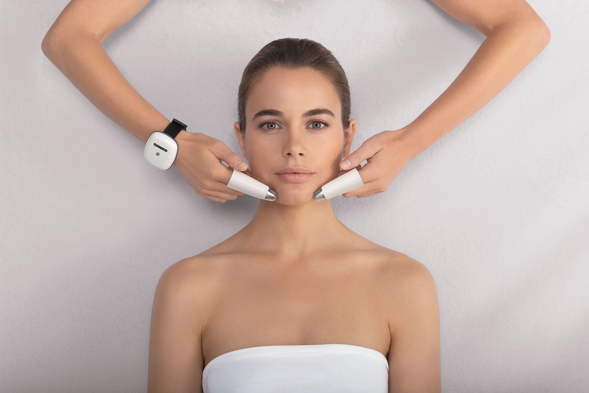 Femme en haut blanc recevant un soin du visage par des mains gantées, avec le produit appliqué autour de son visage
