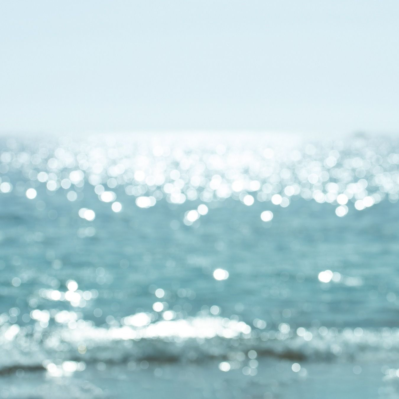 Surface de l’océan baignée de soleil, avec des vagues scintillantes sous un ciel pâle