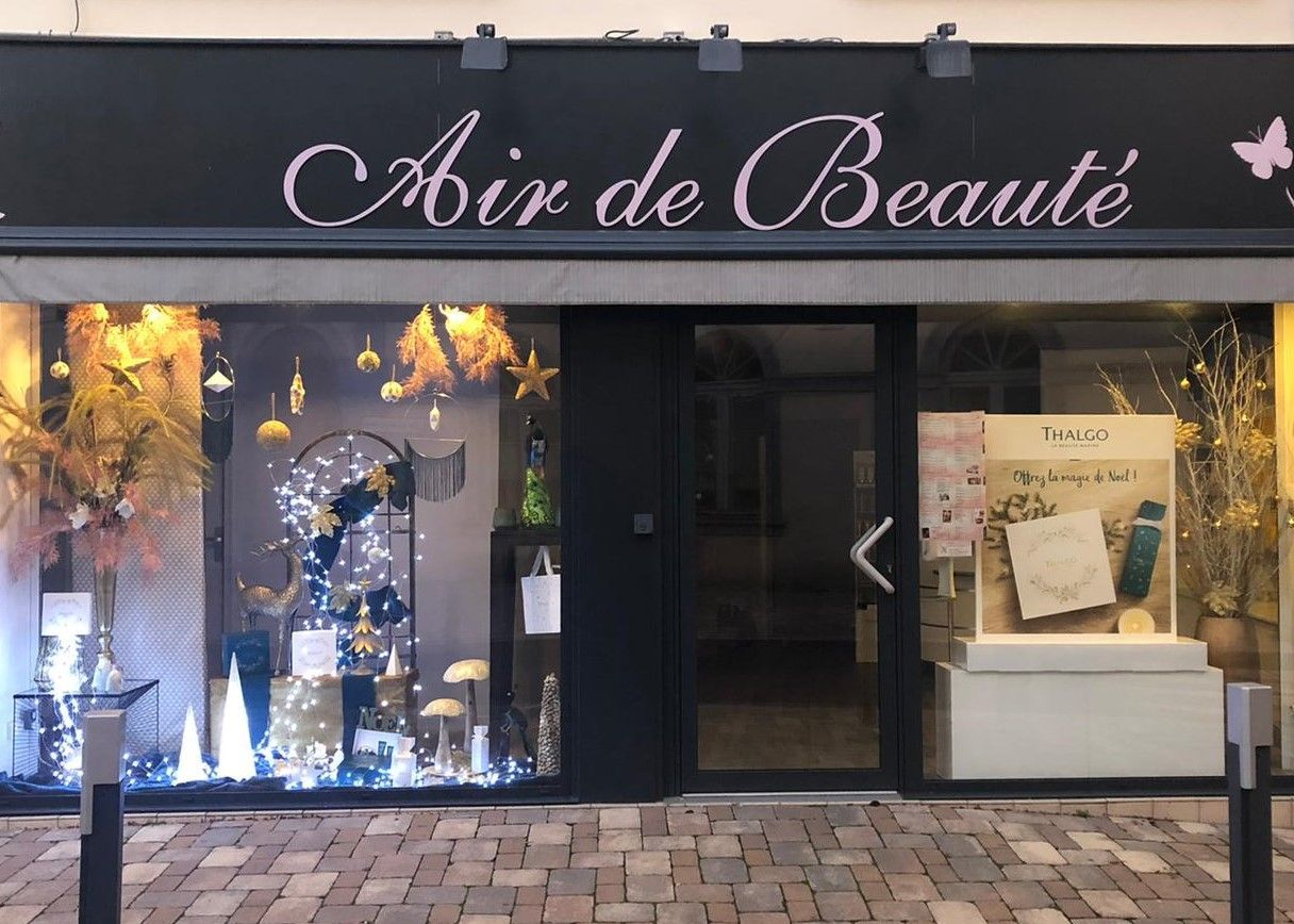 Une boutique avec un store noir sur lequel on peut lire « Aix de Beauté », des vitrines et une entrée éclairée au crépuscule