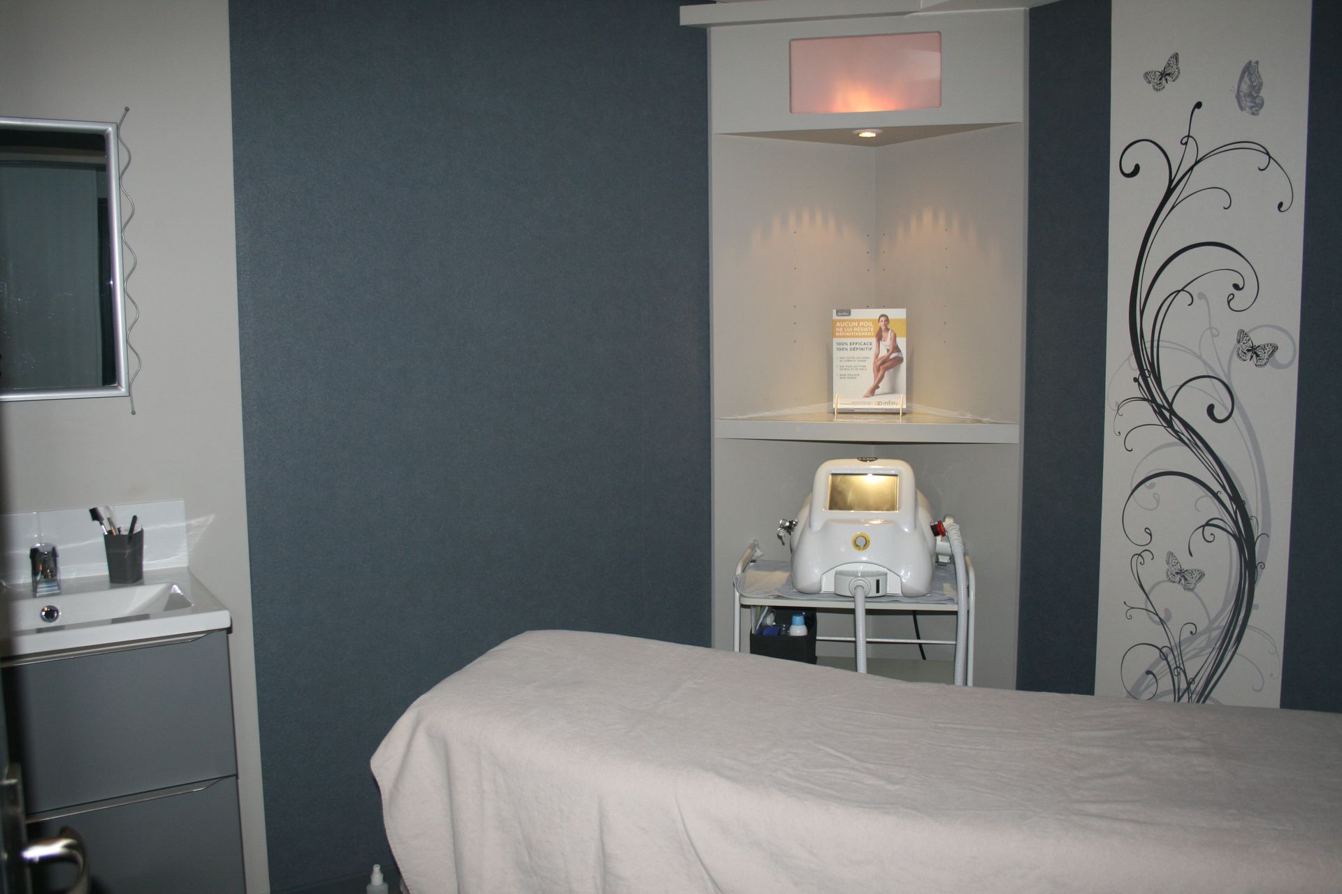 Salle de soins avec une table de massage, des étagères murales et des murs gris décoratifs