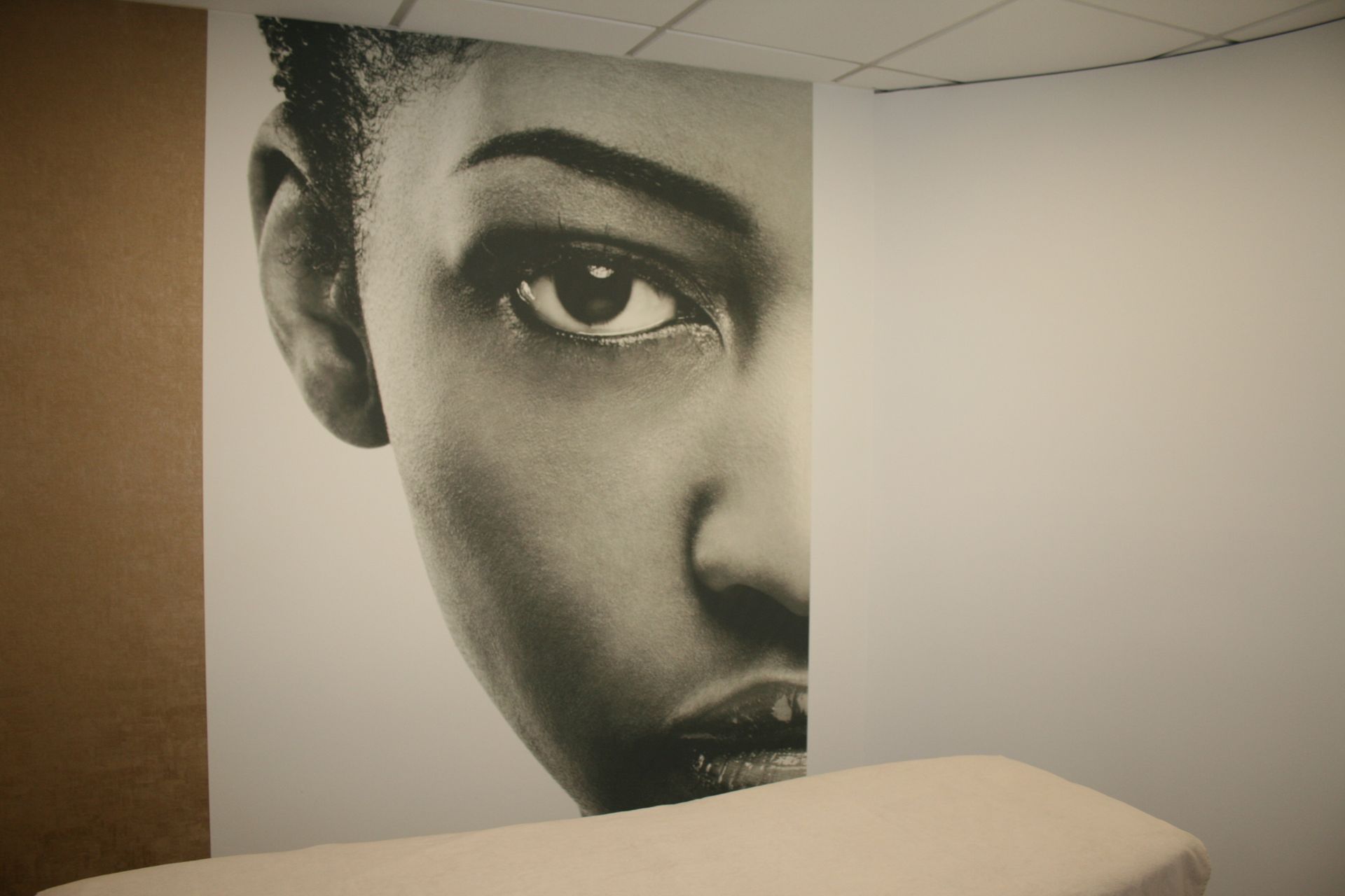 Fresque en noir et blanc représentant un visage avec un seul œil, sur un mur derrière un lit
