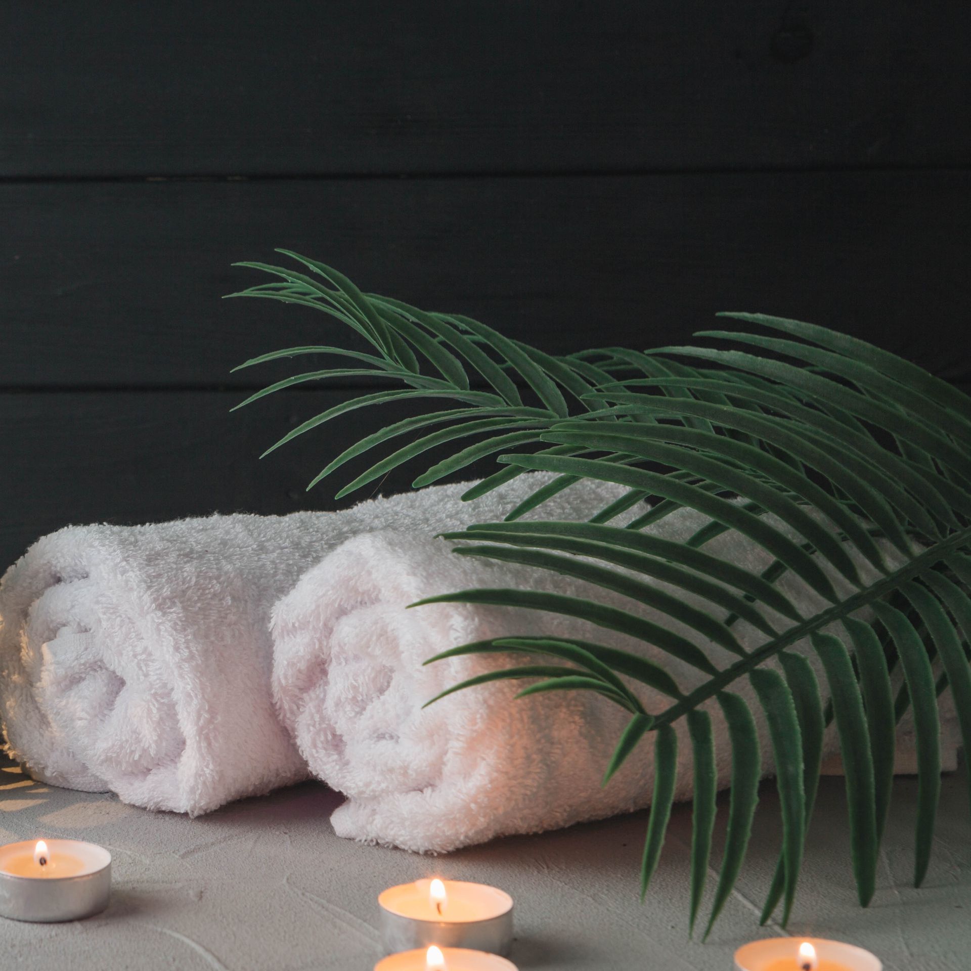 Serviettes blanches roulées, bougies allumées et palme verte sur une table de spa