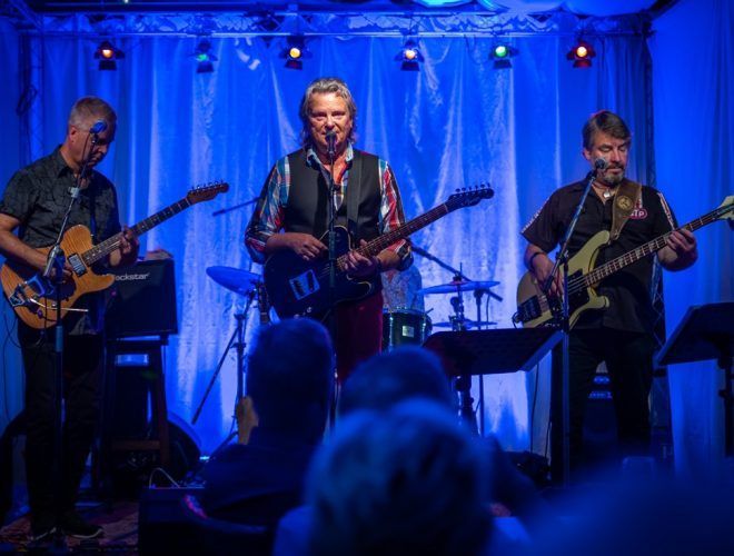 Kolme kitaristia lavalla, sininen lavavalaistus, esiintymässä yleisölle.