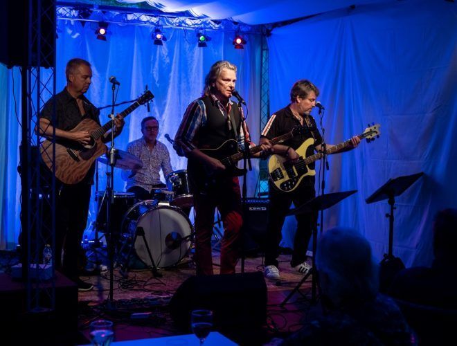 Bändi esiintyy lavalla sinisen valaistuksen alla; laulaja, kitaristit ja rumpali.