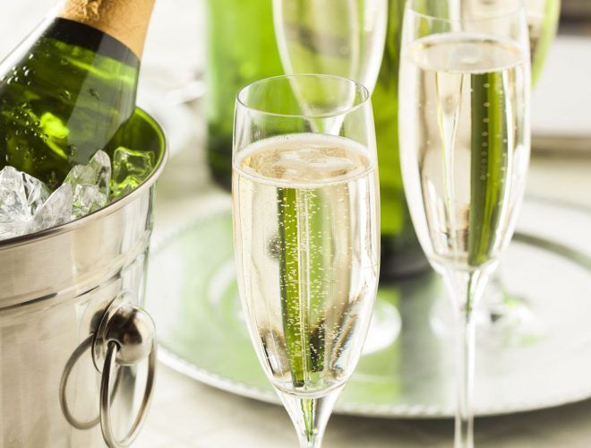 Samppanjapullo jääkaapissa, täytetyt lasit hopeisella tarjottimella, vihreä pullo taustalla.