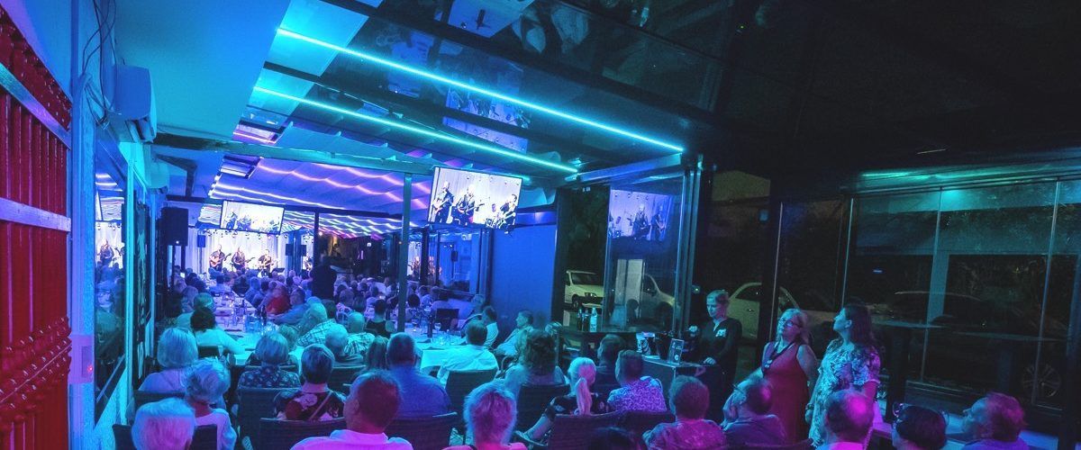 Vilkas tapahtuma paikassa, jota valaisevat siniset ja violetit valot. Ihmiset istuvat, todennäköisesti katsovat esitystä.