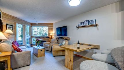 Cozy living room with wood paneling, sofa, chairs, fireplace, and small table.