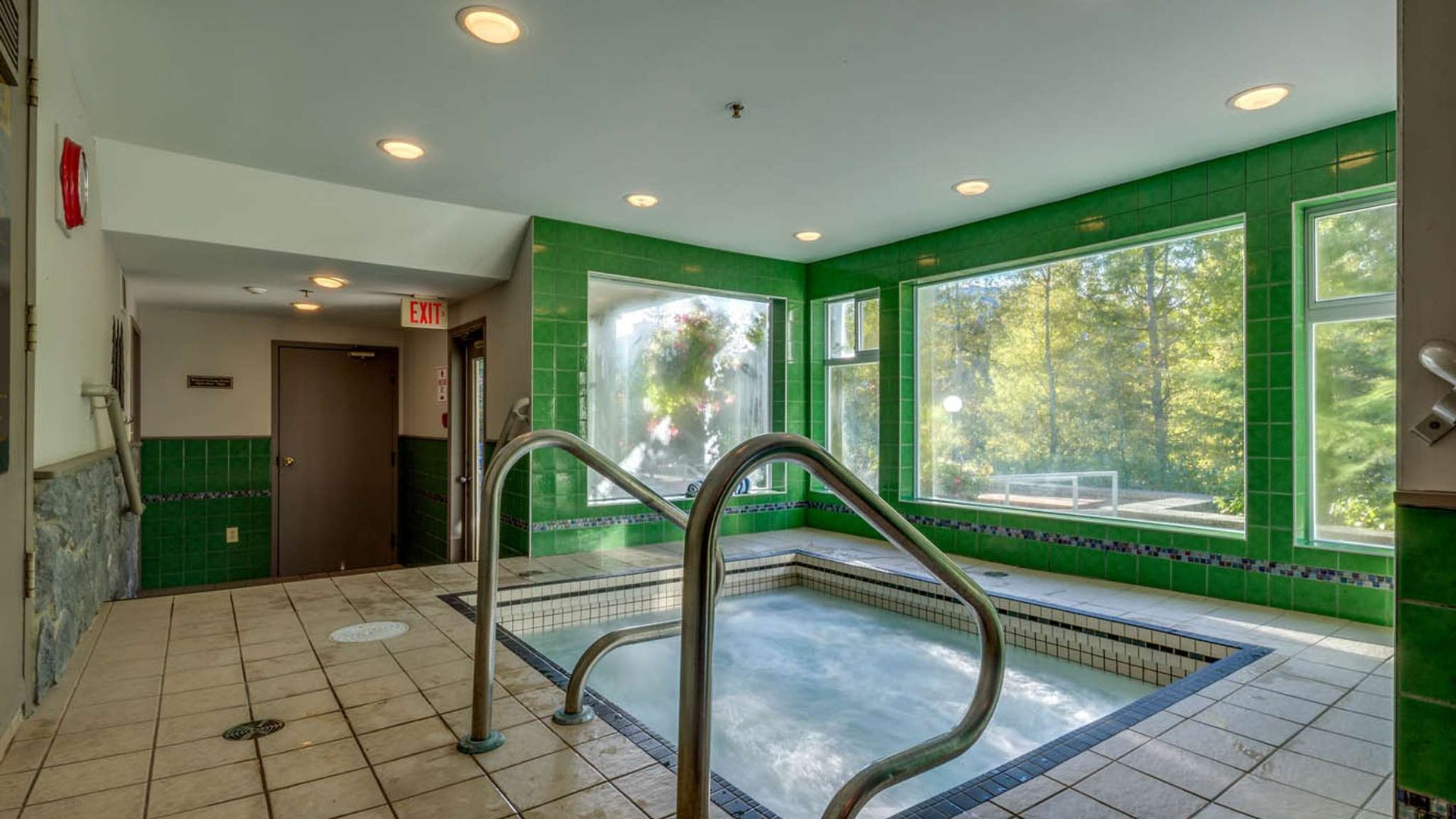 Indoor hot tub area with green walls, large windows, and stainless-steel handrails