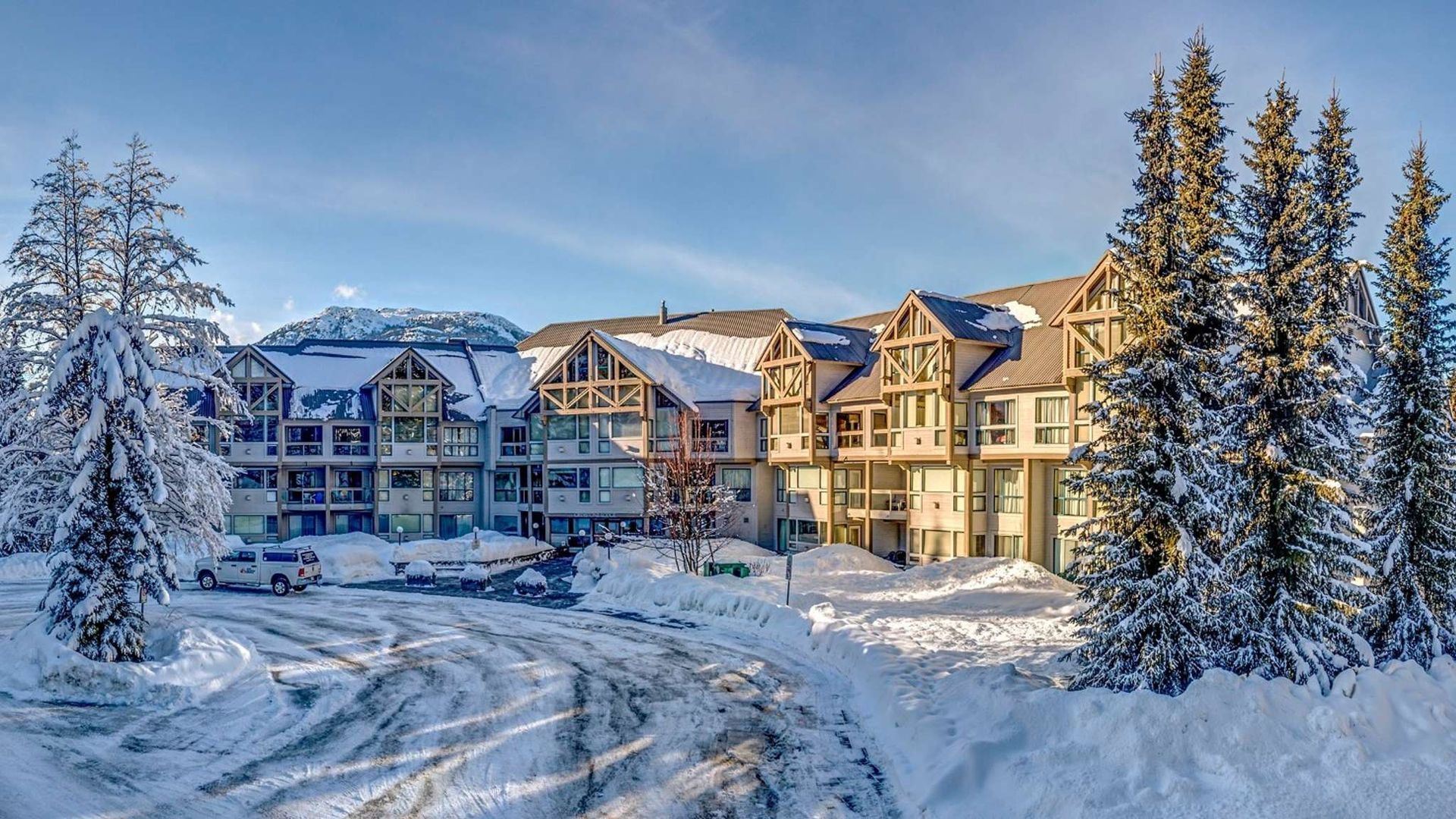 Snow-covered ski resort buildings and pine trees under a clear blue sky.