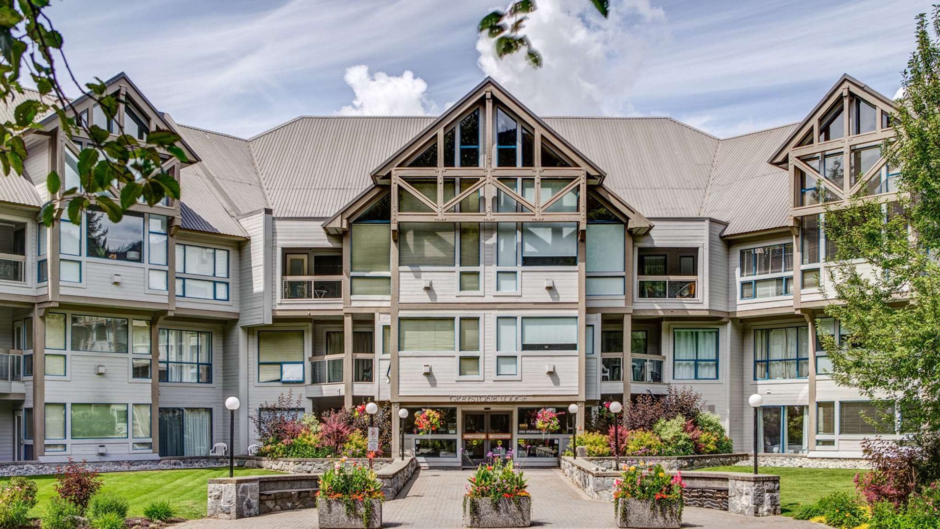 Modern apartment building with gray siding, gabled roofs, and landscaped flower beds in front