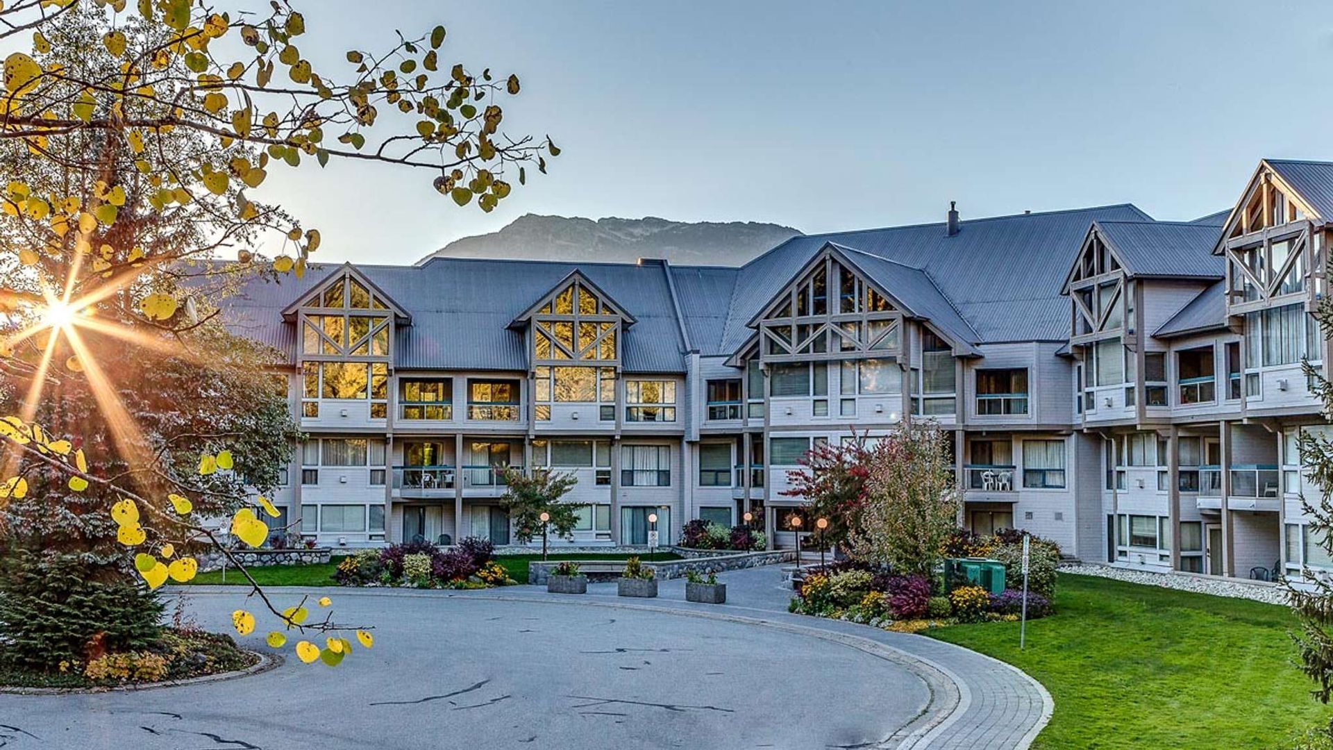 Sunlit stone-and-timber resort lodge with balconies and landscaped courtyard at dusk