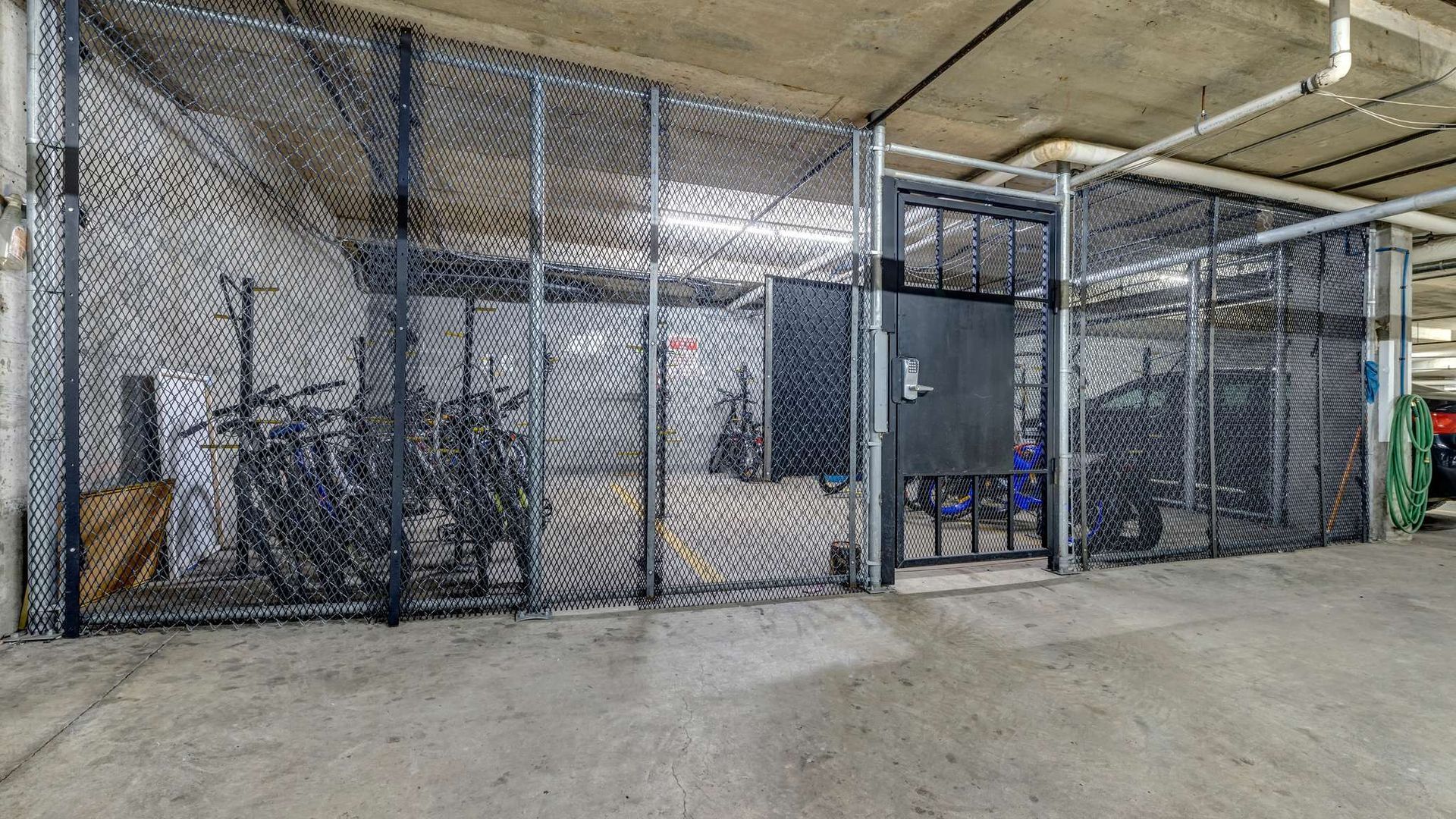 Chain-link storage cages in an industrial warehouse, with bikes and equipment behind the fencing.