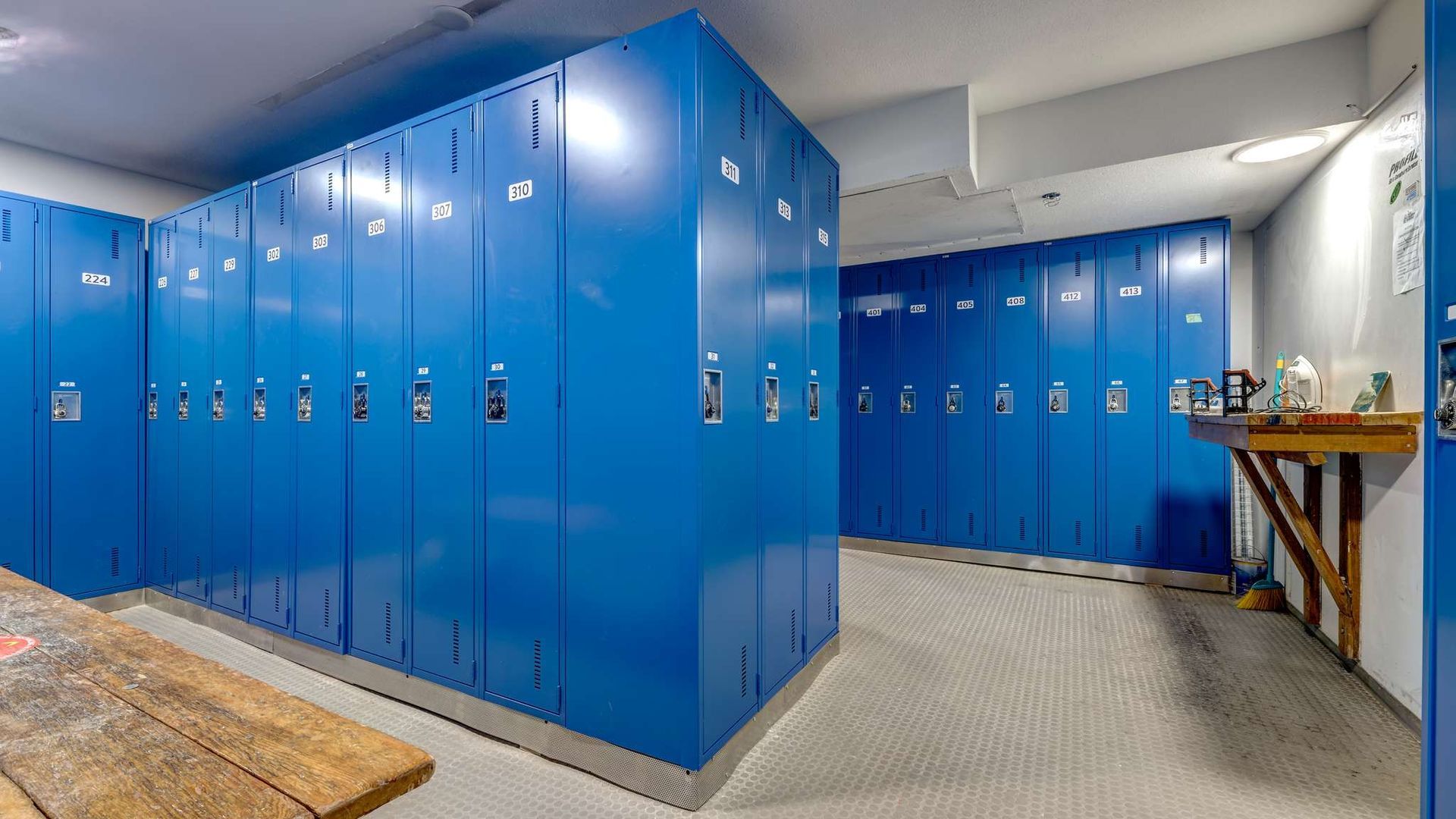 Row of bright blue gym lockers along a white-walled hallway with a table in the foreground