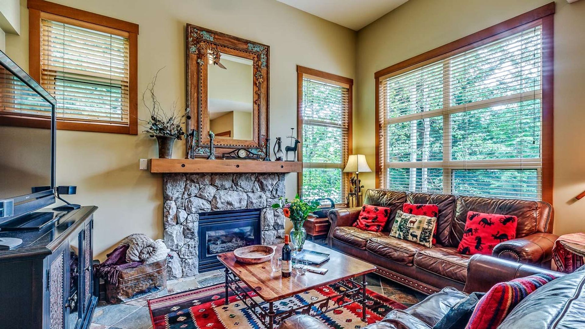 Cozy living room with red patterned sofa, fireplace, mirror, and large windows with blinds